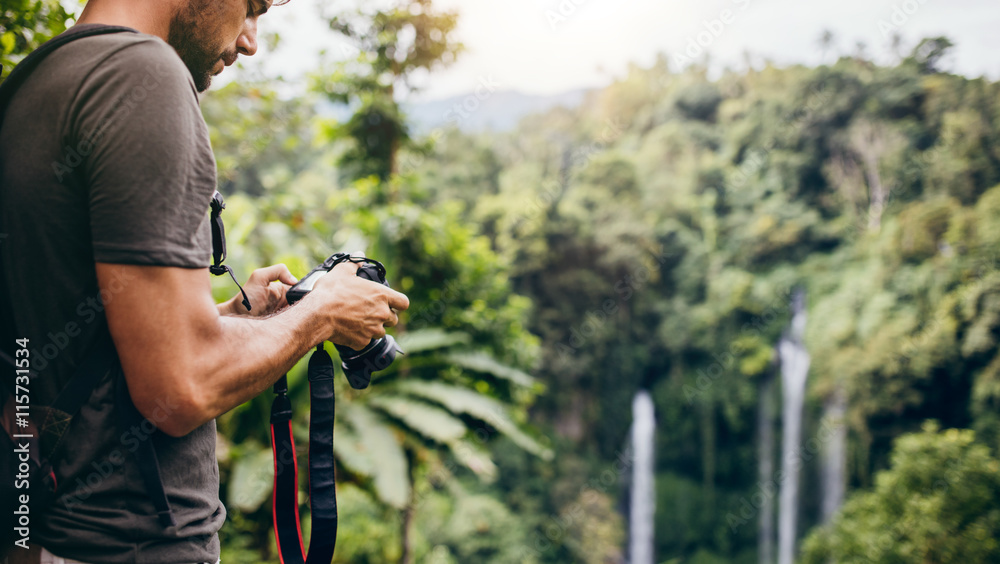 Fotografie Young man with camera by a waterfall in forest