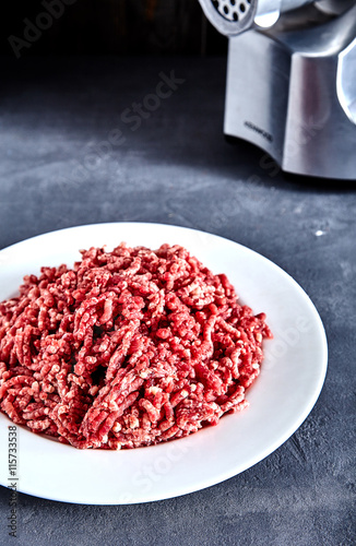 Raw ground beef on a white plate with meat grinder