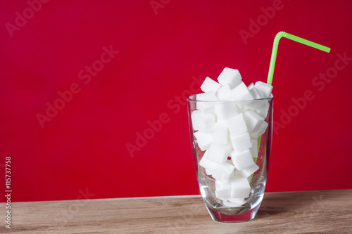 Glass with straw full of sugar and sugar cubes on red background