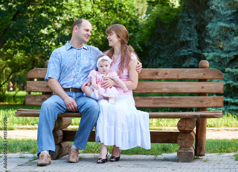 happy family portrait with baby girl on outdoor, sit on wooden bench in city park, summer season, child and parent