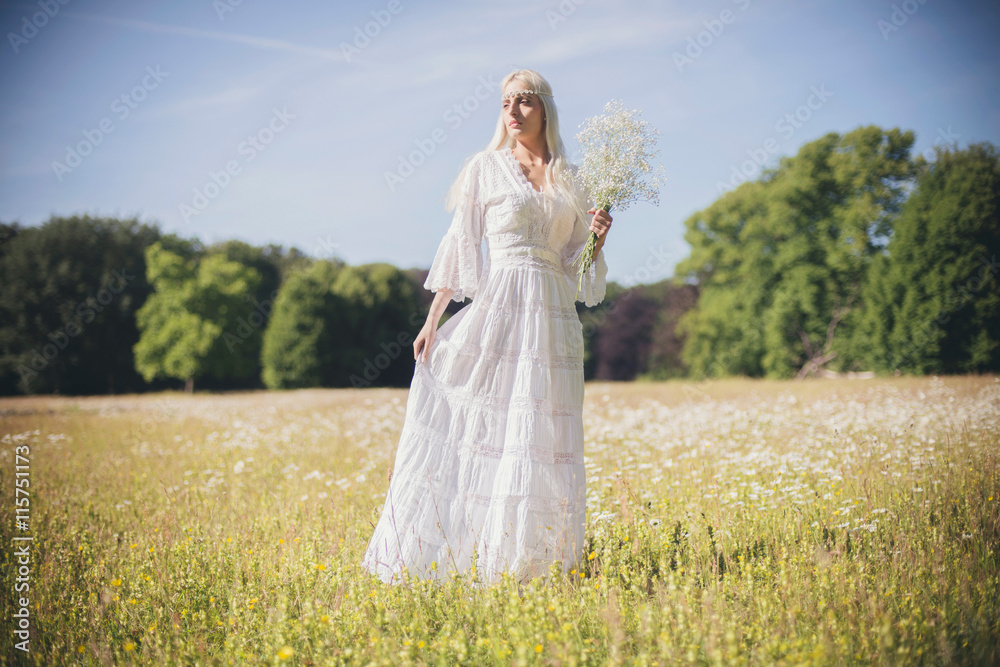 Bride holding white flowers standing in field during summer