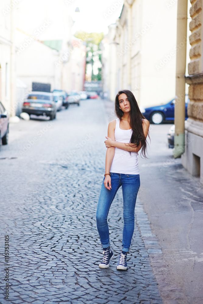 brunette girl n a white T-shirt and blue jeans and is in the city
