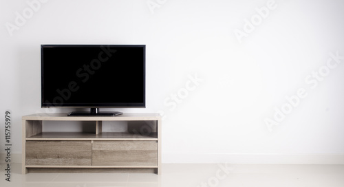 Television put on wood table, background white wall.