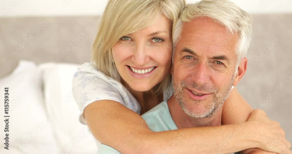 Couple embracing and smiling at camera in bed together Couple embracing and smiling at camera in bed together