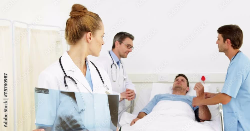 Doctors speaking with sick patient in bed while one checks xray Doctors speaking with sick patient in bed while one checks xray