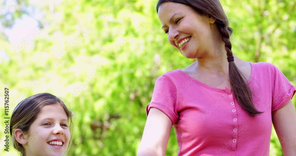 Smiling mother and daughter on a bike ride in the park together Smiling mother and daughter on a bike ride in the park together