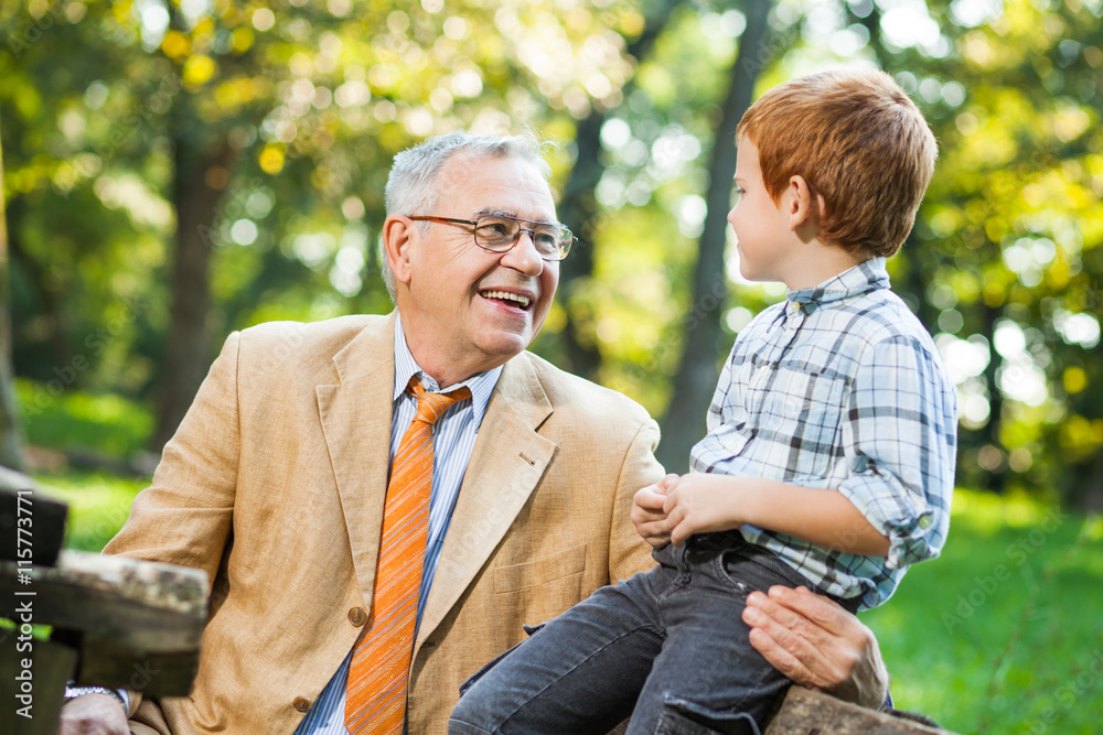 Grandfather and grandson are sitting and talking in park Grandfather and grandson are sitting and talking in park