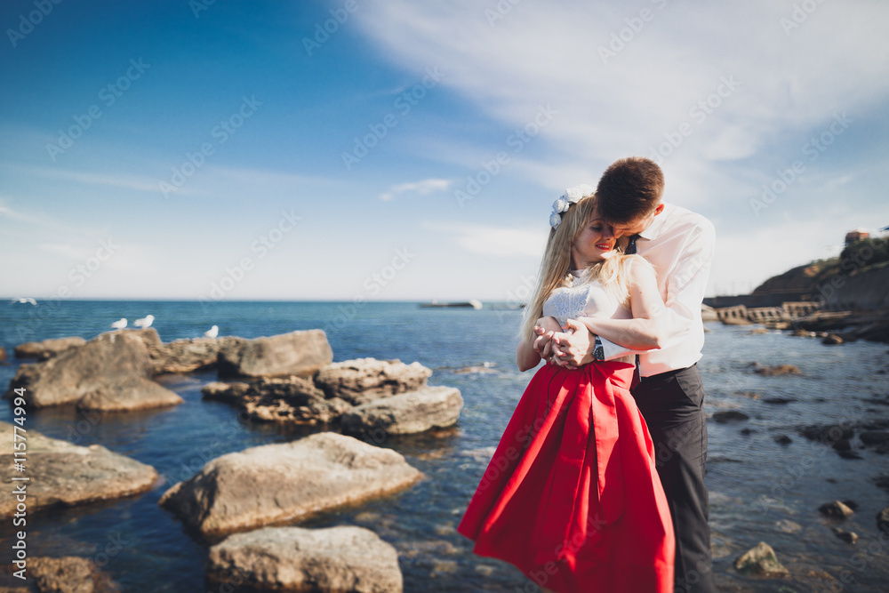 Romantic loving couple posing on stones near sea, blue sky