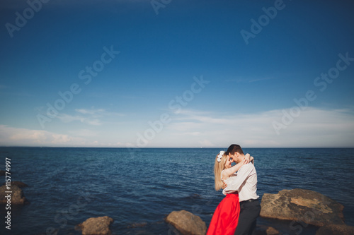 Romantic loving couple posing on stones near sea, blue sky © olegparylyak