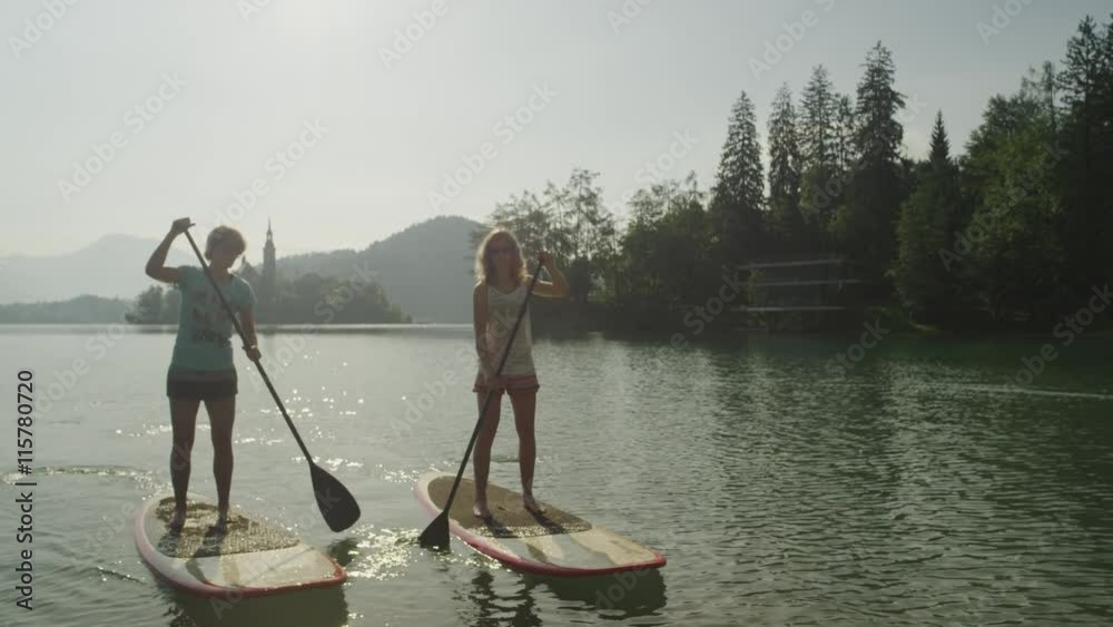 SLOW MOTION CLOSE UP: Girl friends oaring on stand up paddle boards