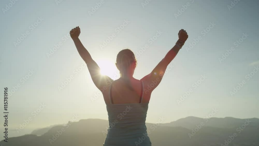 Young woman raising hands on the edge of ocean cliff