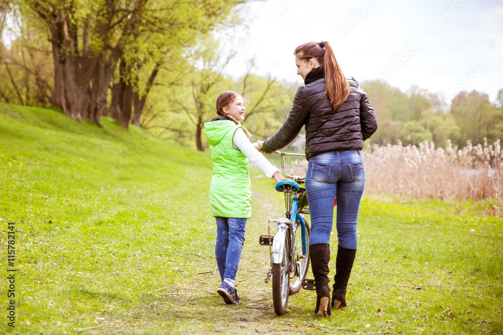 Daughter and mother walk along the shore of the lake with a bike and talk. Family values, education Daughter and mother walk along the shore of the lake with a bike and talk. Family values, education