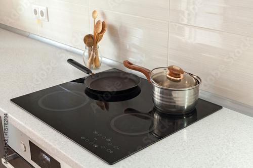 Open saucepan, pan and wooden spoons in modern kitchen with induction stove