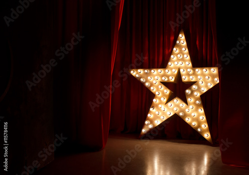 Εκτύπωση καμβά Photo of golden star with light bulbs on red velvet curtain on stage