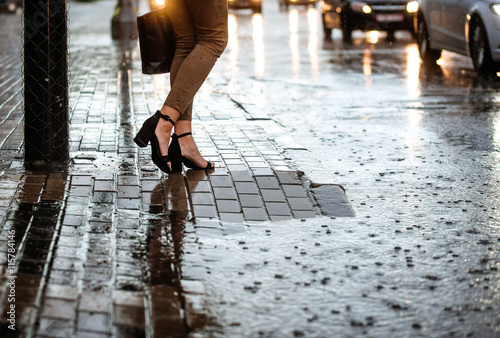 Woman crosses wet street with large pool. Closeup legs. Heavy rain.