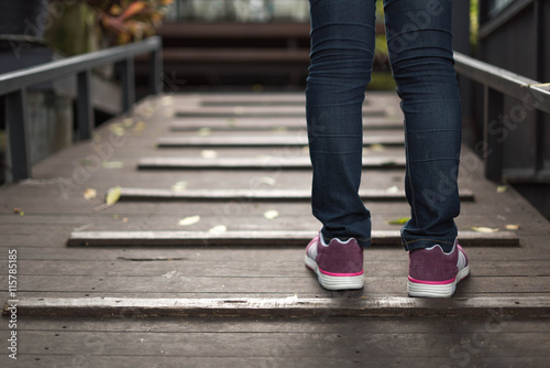women wearing jeans and sneakers step on old wooden bridge
