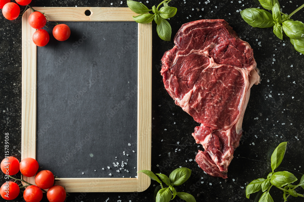 Fresh steak served with spices, tomatoes and leafs of basil on marble background. Uncooked beefsteak cooking on a kitchen. Delicious, spicy, juicy meat with copy space closeup.