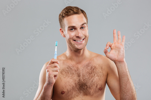 Happy young man holding toothbrush and showing ok sign photo