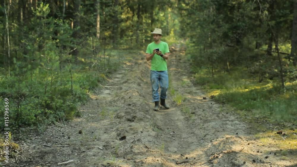 A man walks through the forest with the phone and looks at the navigation application. He chooses the right direction A man walks through the forest with the phone and looks at the navigation application. He chooses the right direction
