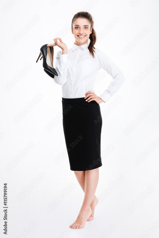 Fototapeta premium Smiling young businesswoman standing barefoot and holding high heels shoes