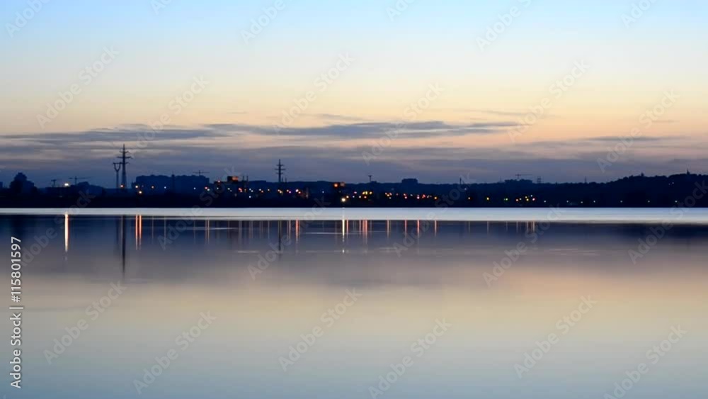 Time lapse of nightfall in the city near shore with city lights turning on far off and landscape changing from day to night Time lapse of nightfall in the city near shore with city lights turning on far off and landscape changing from day to night