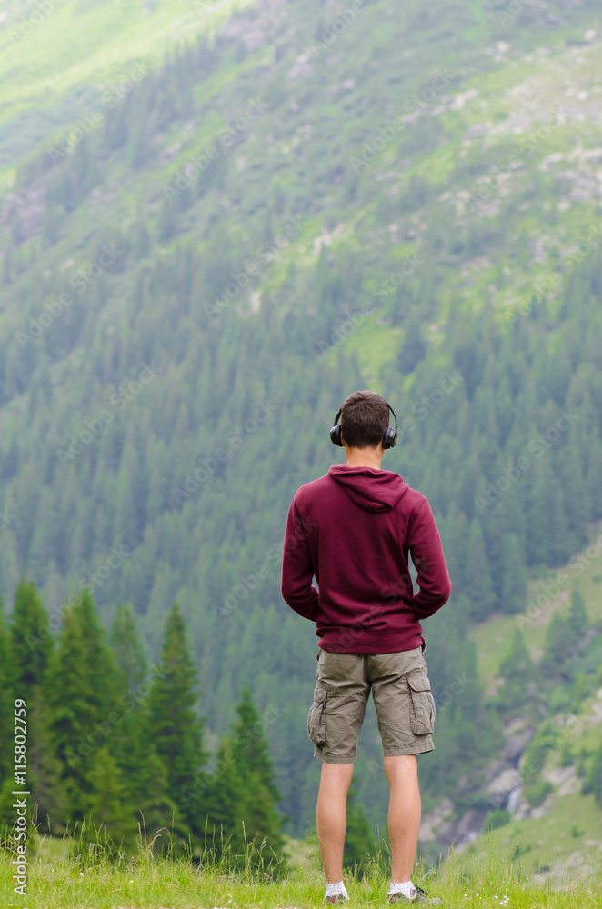 Back of teenager listen to music at headphones on mountain