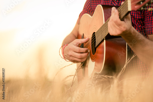 Close up of male hands playing acoustic guitar on the wheat field at the sunset. Retro, music, lifestyle concepts.