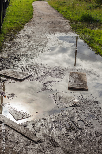 Dirty puddle on a country road with the reflection of sky and clouds.