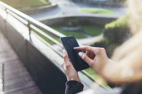 Hipster texting message on smartphone or technology, mock up. Tourist girl using cellphone on bridge background close. Female hands holding gadget blurred backdrop. Mockup space for message or design