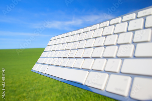 Computer keyboard on sky and grass background