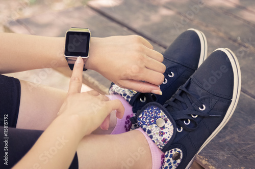 High angle view of female forefinger pressing the button on smart watch with blank screen while sitting on a bench in the park. 