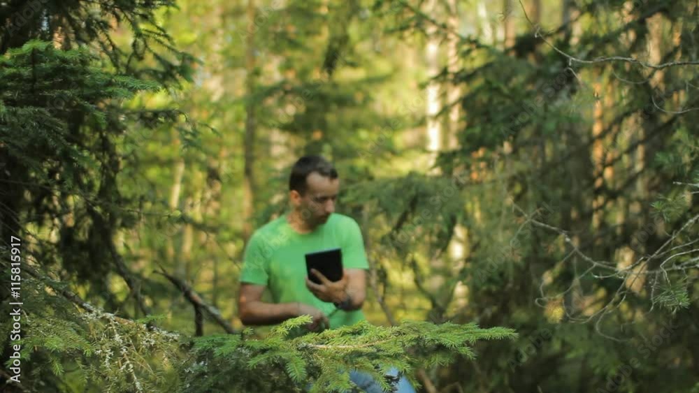 A man walks through the forest with a tablet PC and looking at the navigation application. He chooses the right direction A man walks through the forest with a tablet PC and looking at the navigation application. He chooses the right direction