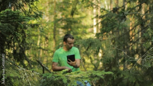 A man walks through the forest with a tablet PC and looking at the navigation application. He chooses the right direction