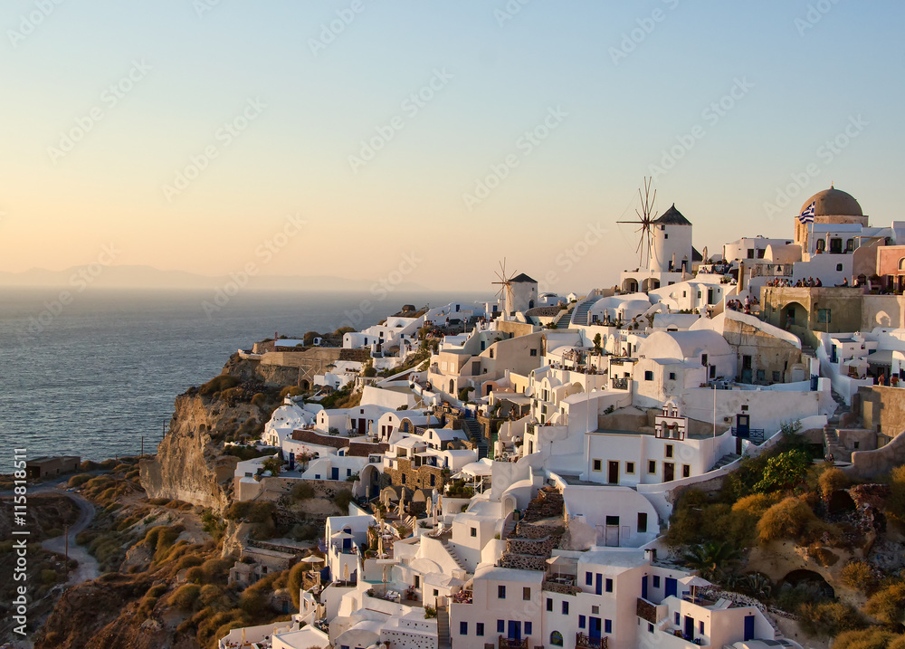 Two white old mills on a background of white plastered houses at sunset in the town of Oia on Santorini island in Greece