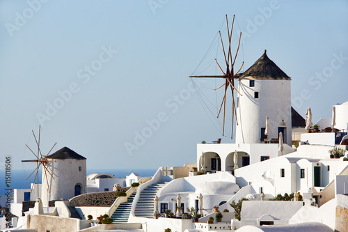 Two white old mills on a background of white plastered houses in the town of Oia on Santorini island in Greece