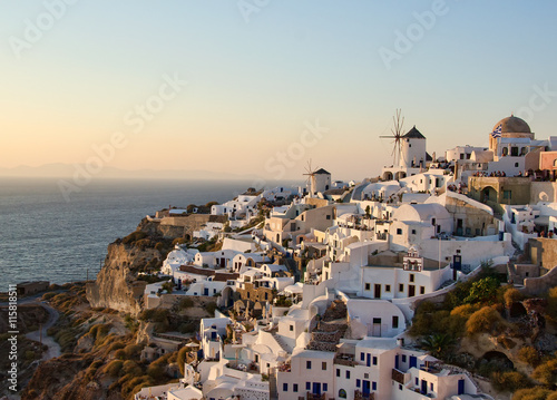 Two white old mills on a background of white plastered houses at sunset in the town of Oia on Santorini island in Greece