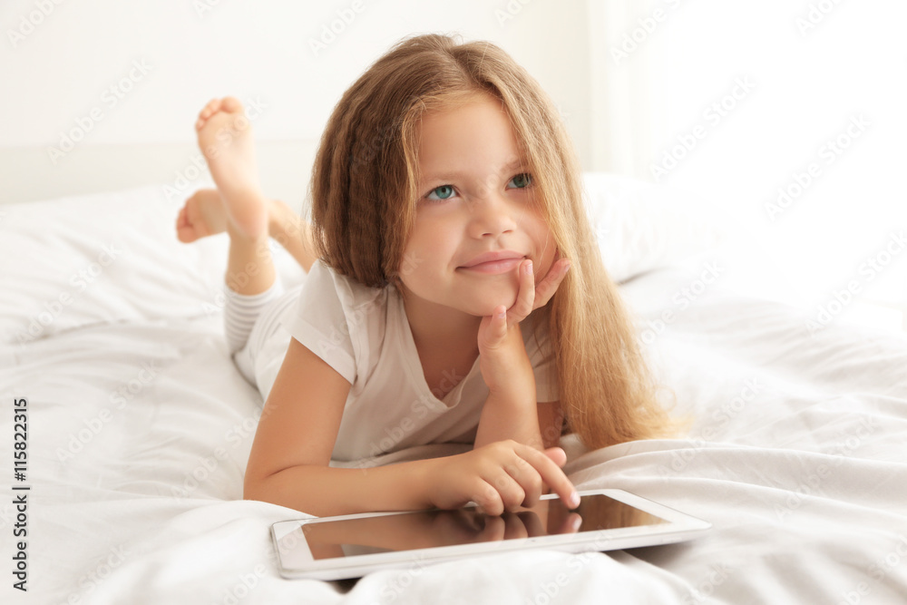 Cute little girl playing with tablet on white bed Cute little girl playing with tablet on white bed