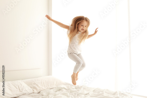 Fototapeta Naklejka Na Ścianę i Meble -  Cute little girl jumping on white bed