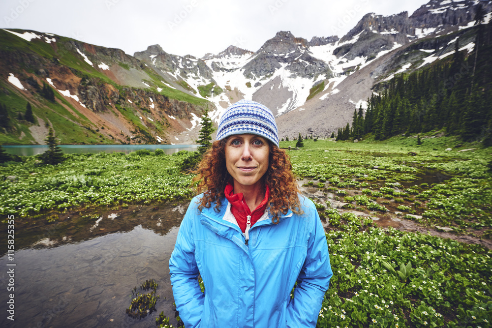 a portrait of a young woman standing in front of mountains