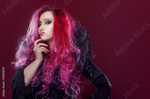 Scary witch with red hair performs magic on a pink background. Halloween, horror theme.