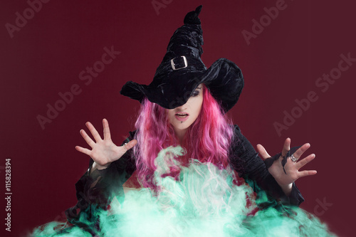 Scary witch with red hair performs magic over the green smoke . Halloween, horror theme.