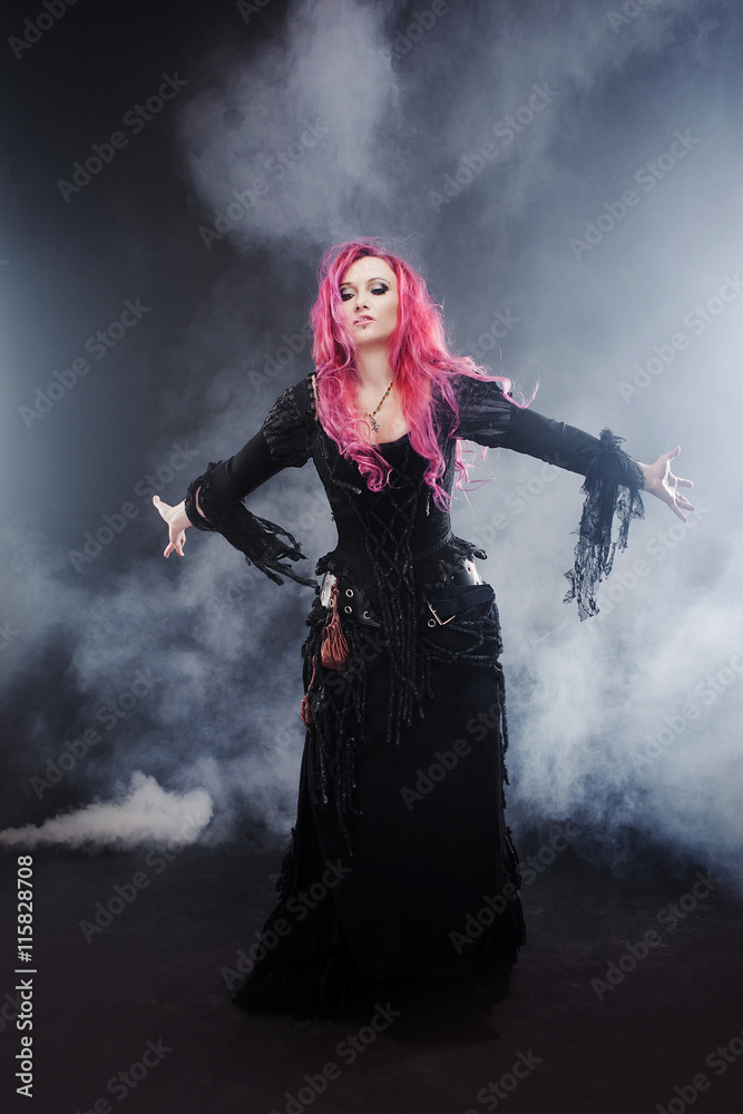 Halloween Witch creates magic. Attractive woman with red hair in witches costume standing outstretched arms, strong wind