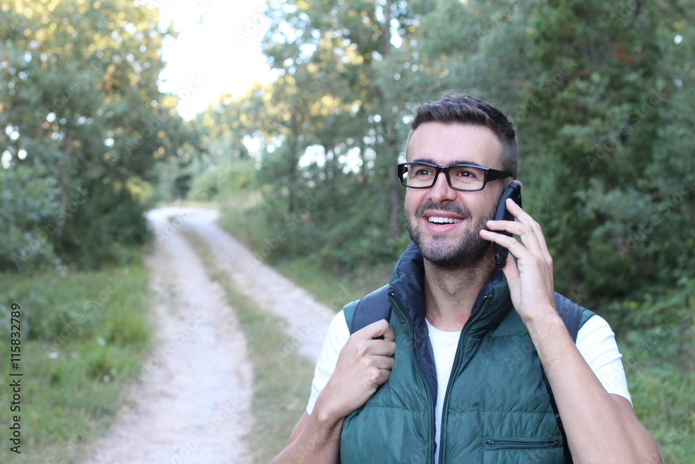 Handsome hiker with glasses talking on mobile phone and looking at away with gorgeous green view of nature Handsome hiker with glasses talking on mobile phone and looking at away with gorgeous green view of nature