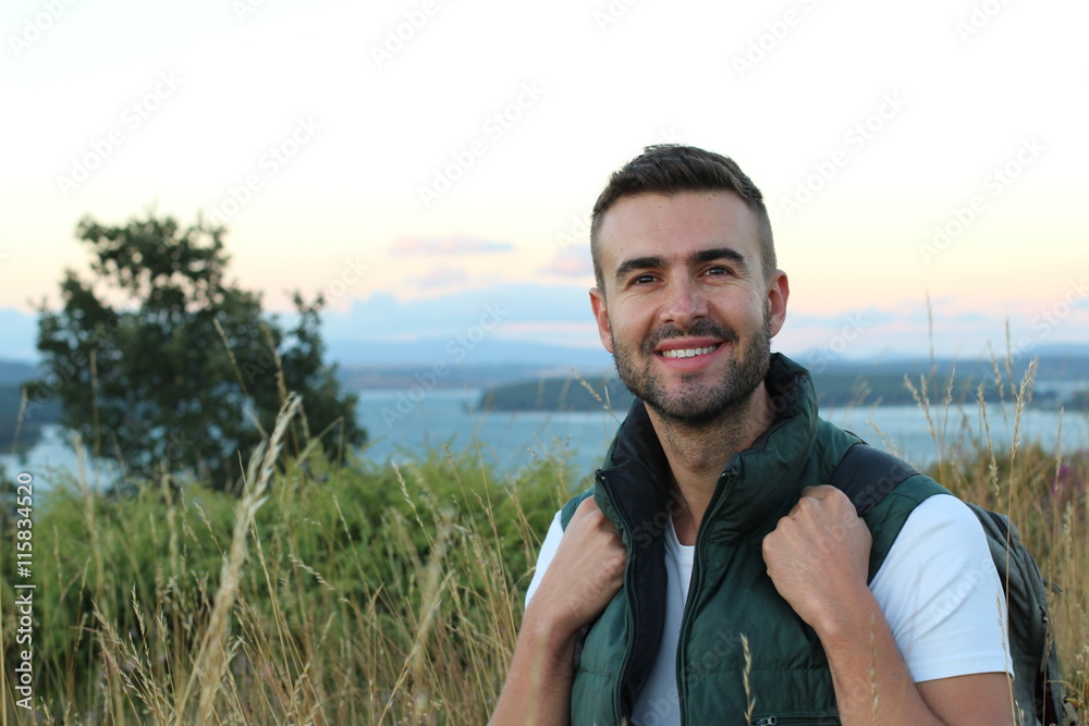 Portrait of a young tourist in mountain clothes and backpack standing on a top of mountain and enjoying scenery landscape view, hiker looking to copy space area for your text message or information Portrait of a young tourist in mountain clothes and backpack standing on a top of mountain and enjoying scenery landscape view, hiker looking to copy space area for your text message or information