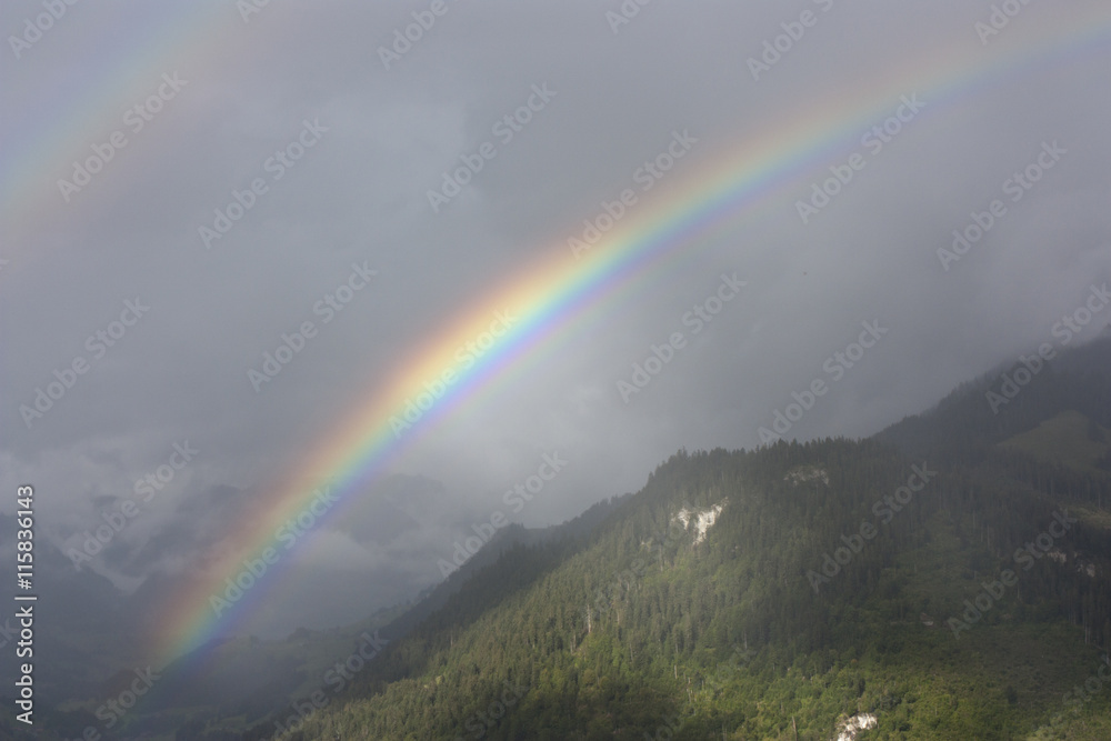 Double rainbow over misty forested hills in Switzerland.