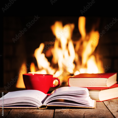 Fotografia Red cup of coffee or tea and old books on wooden table near  fir