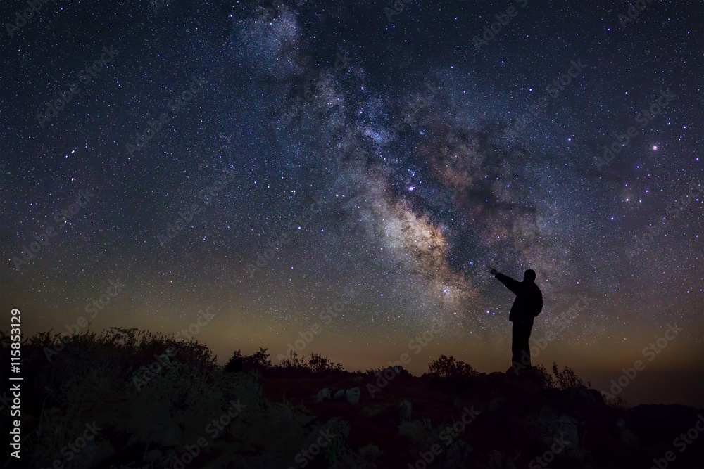 A Man is standing next to the milky way galaxy pointing on a bri