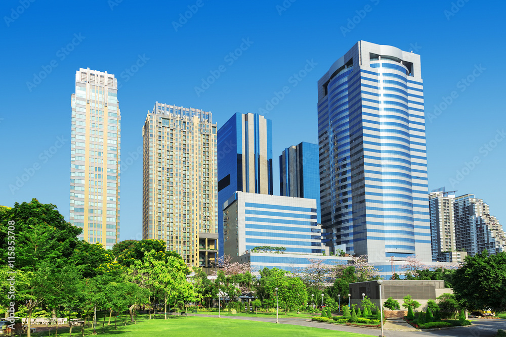 Skyscrapers and blue sky fill the background behind beautiful green grass and trees.