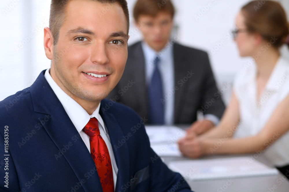 Portrait of cheerful smiling business man against a group of business people at a meeting. Portrait of cheerful smiling business man against a group of business people at a meeting.