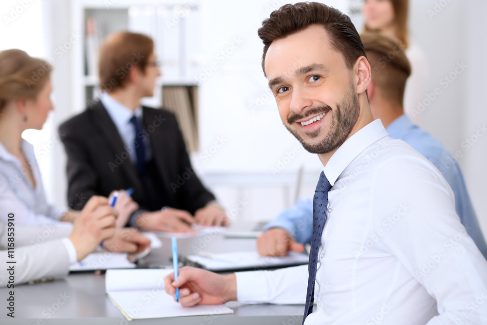 Portrait of cheerful smiling business man against a group of business people at a meeting. Portrait of cheerful smiling business man against a group of business people at a meeting.